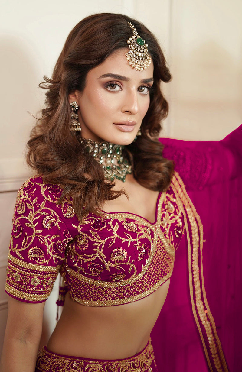 A woman in a boysenberry lehenga set with gold embroidery and a maang tikka.