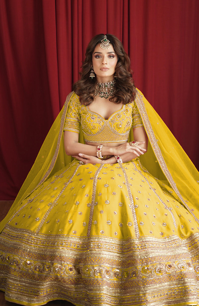A woman in a yellow lehenga set with gold embroidery and a matching dupatta.