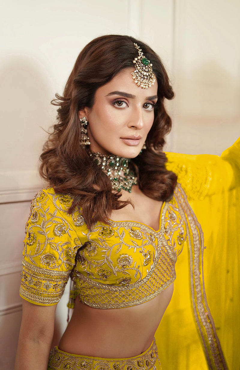 A woman in a yellow embroidered lehenga set with a maang tikka and choker.