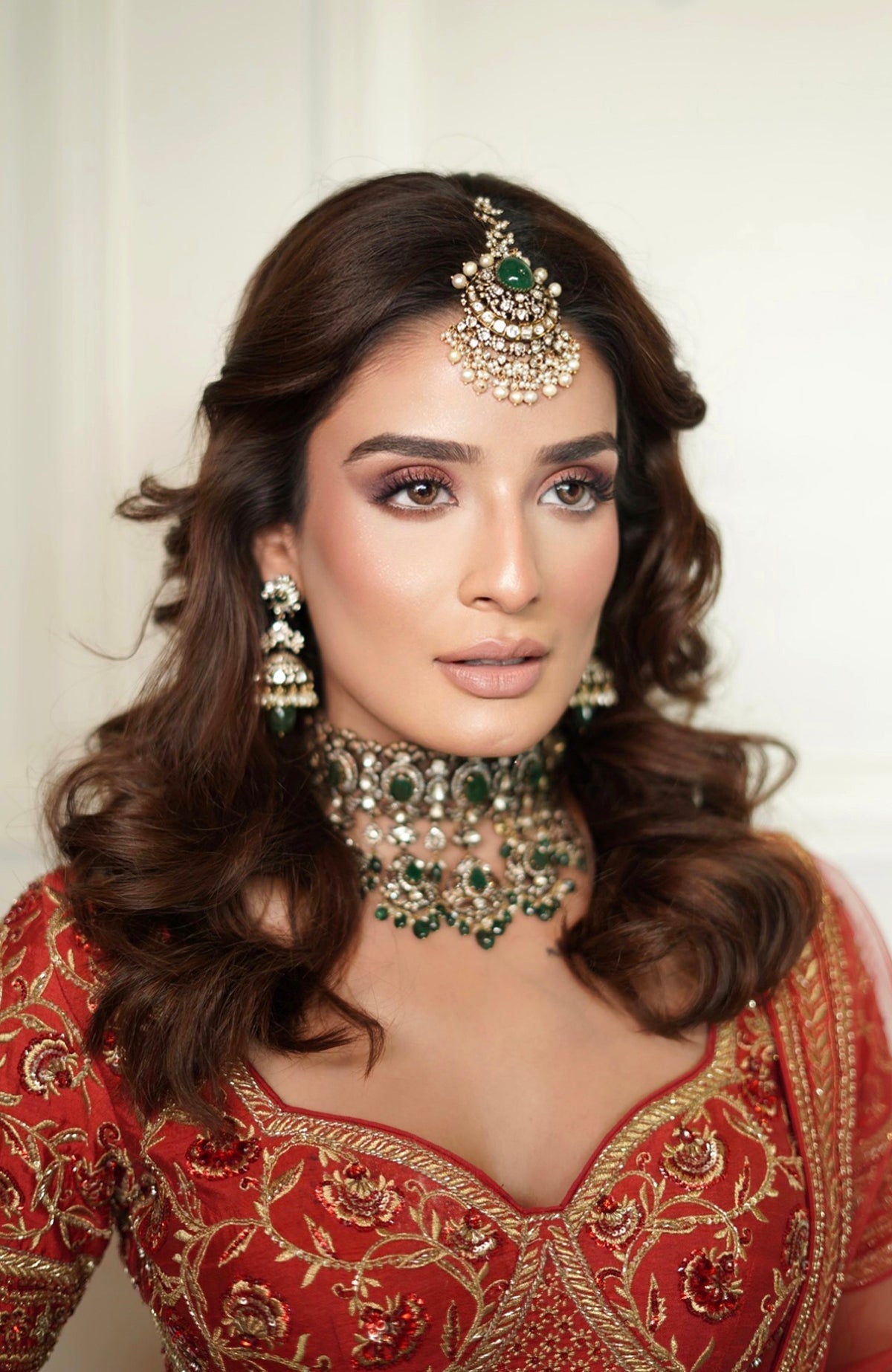 A woman in a red embroidered lehenga set with a choker and maang tikka.