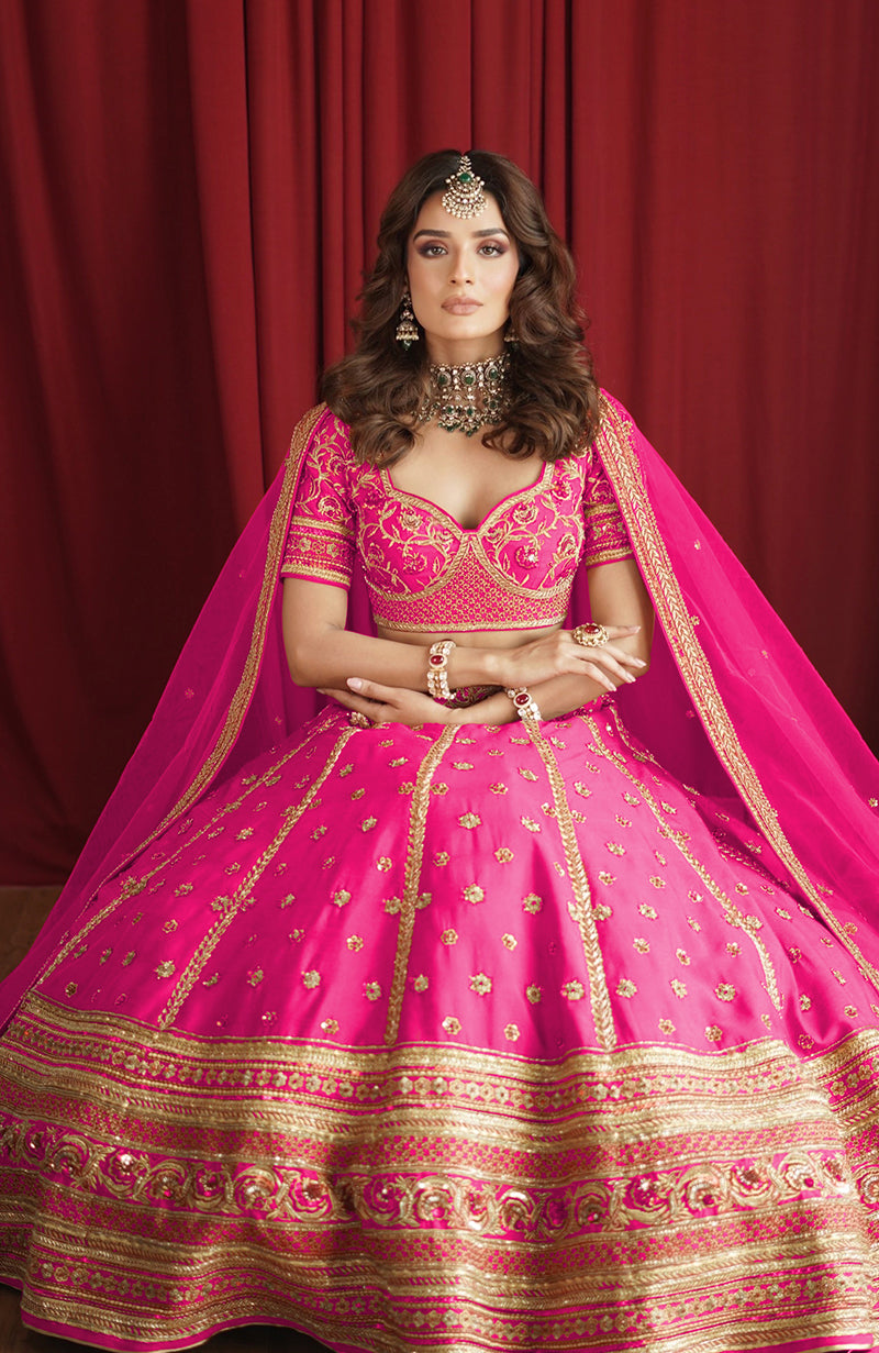 A woman in a fuchsia lehenga set with gold embroidery and traditional jewelry.