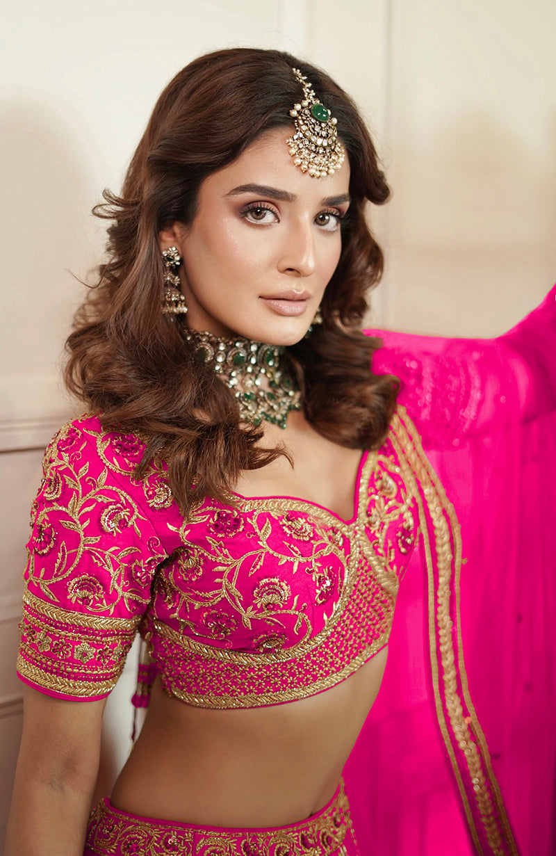 A woman in a fuchsia lehenga set with gold embroidery and traditional jewelry.
