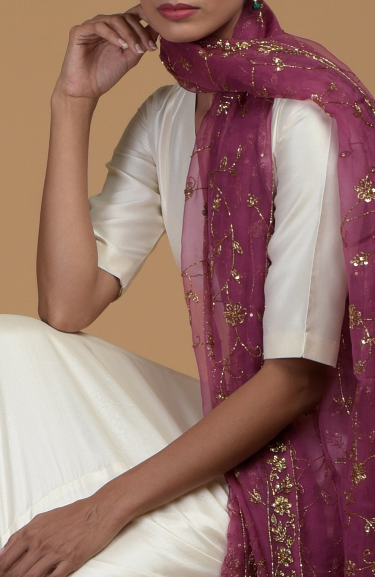A woman in an ivory suit and a pink embroidered dupatta poses with her hand on her chin.