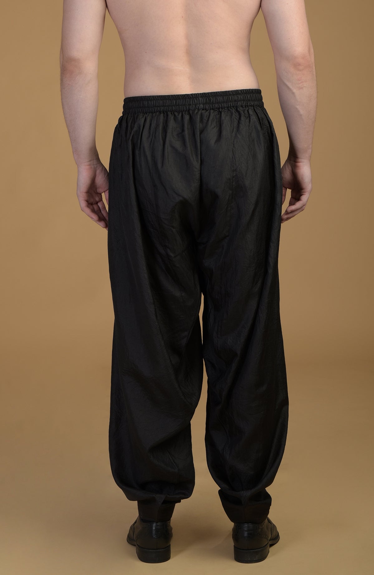 A person from behind wears black silk salwar pants with an elasticated waist.