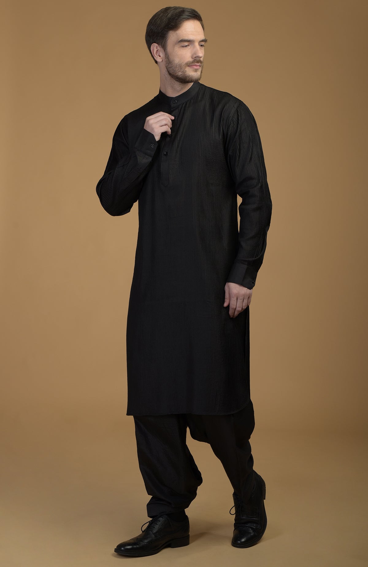 A man models a black silk Pathani kurta set with pintuck details and salwar pants.
