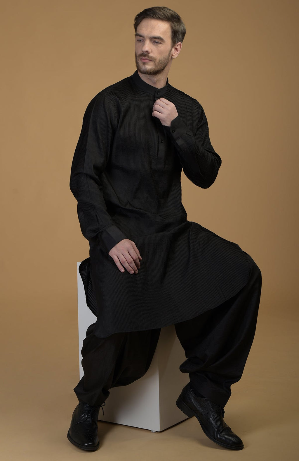 A man models a black silk Pathani kurta set with pintuck details.