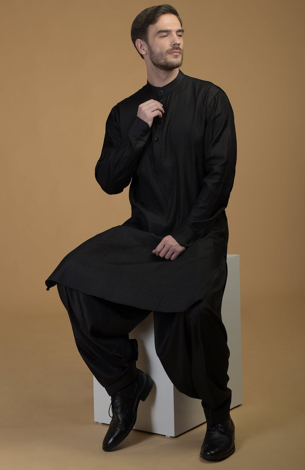 A man models a black silk Pathani kurta set with pintuck details.