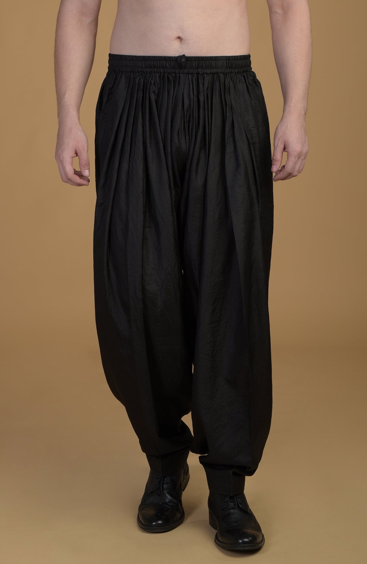 A person models black silk pathani salwar pants with a gathered waist and black shoes.