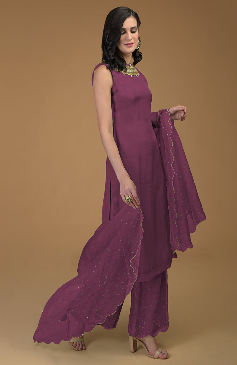 A woman models a burgundy purple kurta set with zardozi embroidery and scalloped hems.