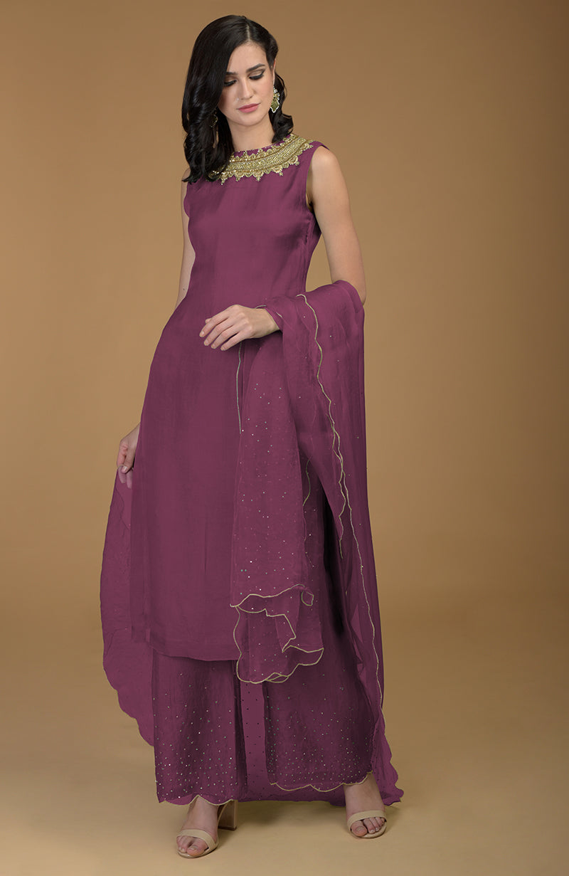A woman models a purple kurta set with gold embroidery and embellishments.