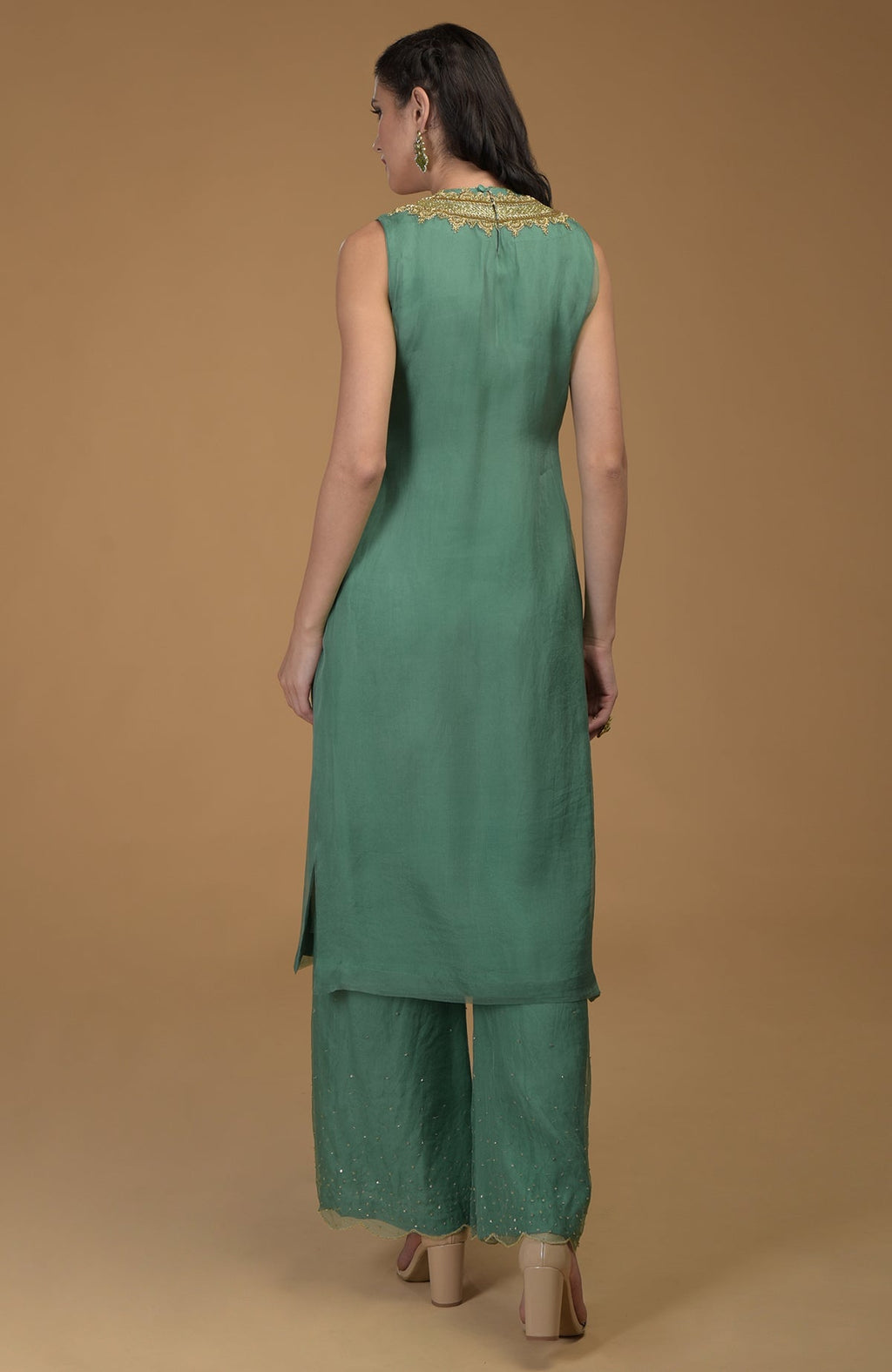 Rear view of a woman in a green sleeveless kurta set with gold embroidery.