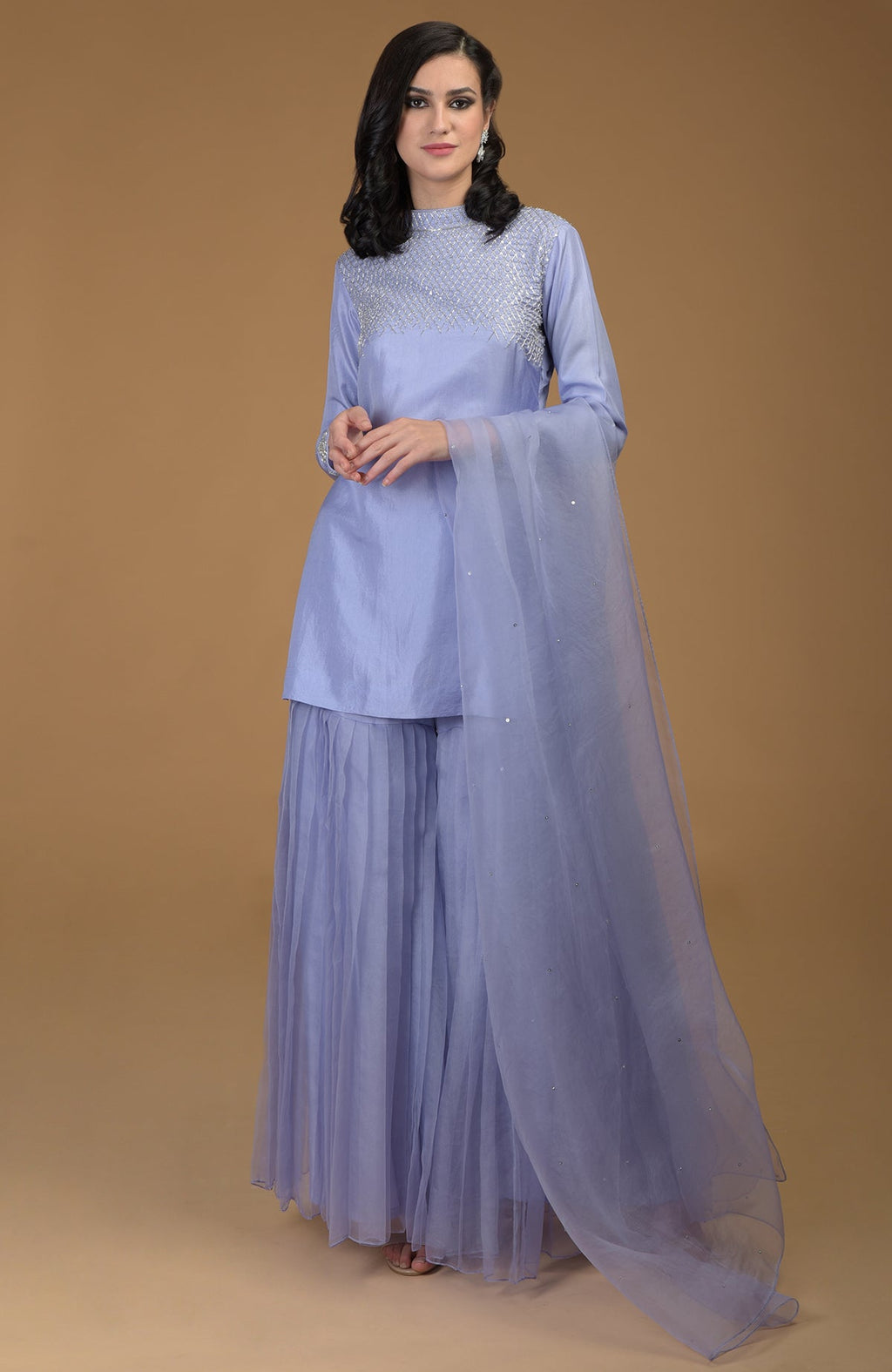A woman models a pastel lilac gharara set with zardozi embroidery and a sheer dupatta.