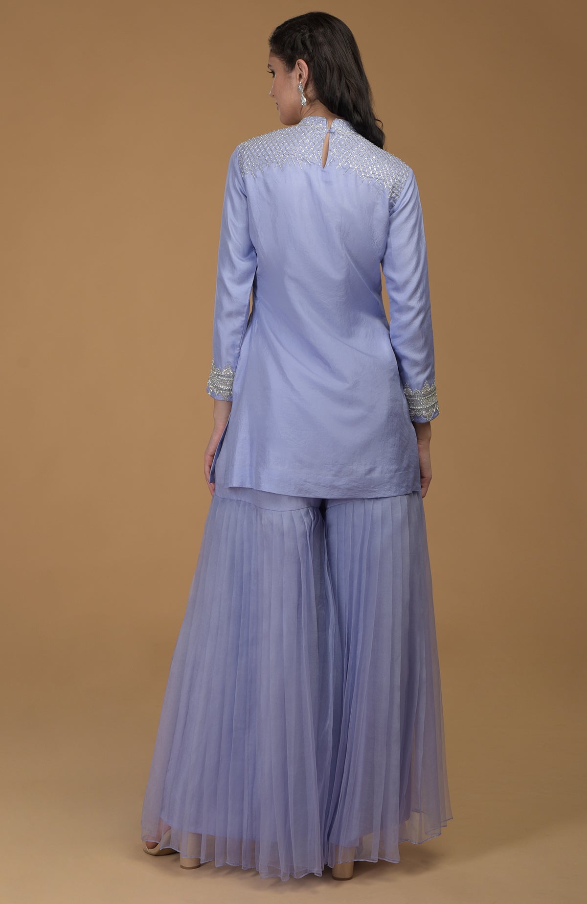 A woman from behind wearing a pastel lilac kurta with embroidered yoke and pleated gharara.