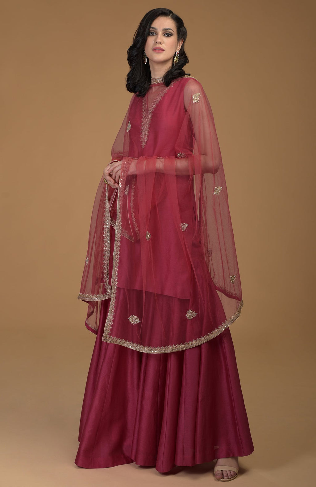A woman models a ruby red zardozi hand-embroidered gharara suit with a sheer dupatta.