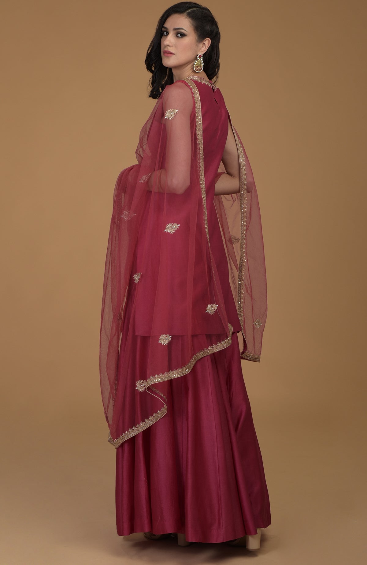 A woman models a ruby red gharara suit with gold zardozi embroidery.