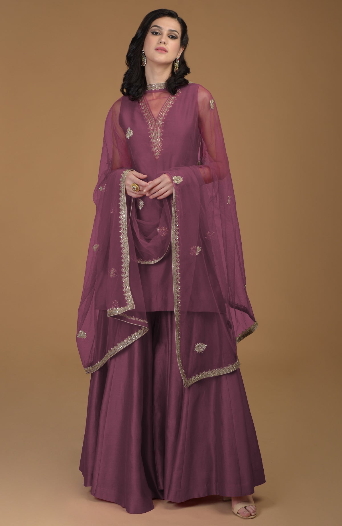 A woman models a ruby red zardozi hand-embroidered gharara suit with a sheer dupatta.