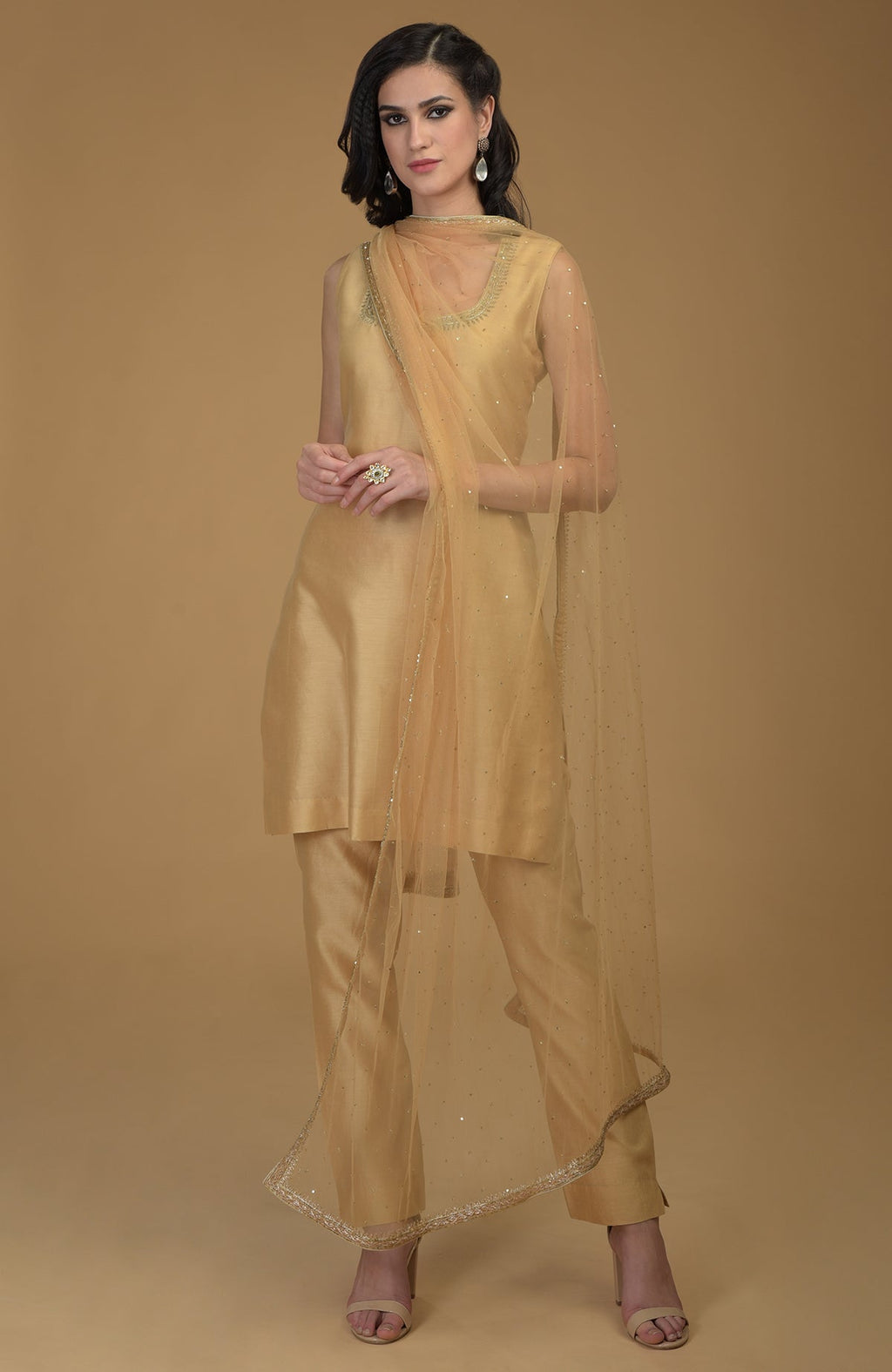 A woman models a nude gold zardozi hand-embroidered suit with a sheer dupatta.