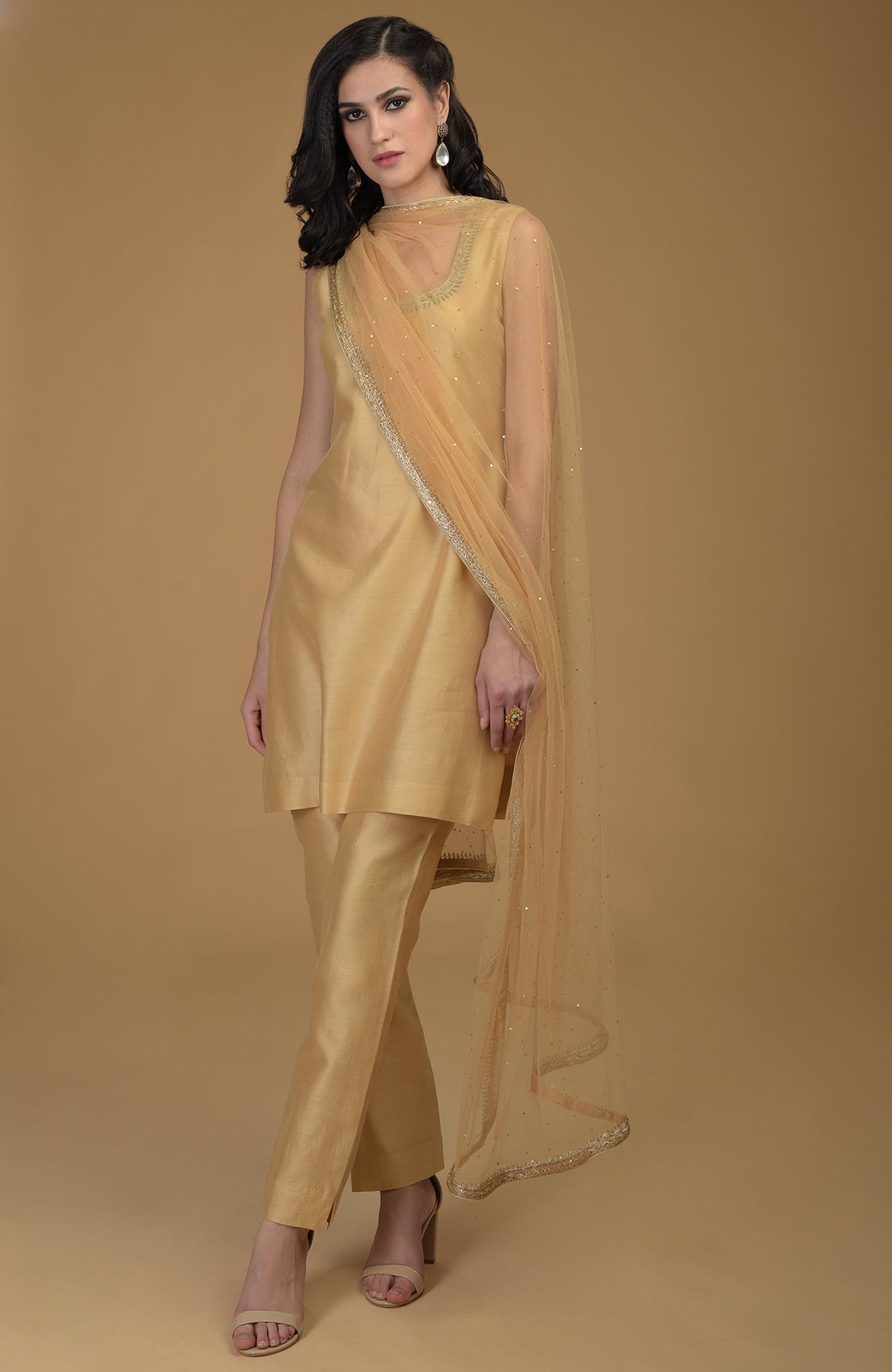A woman models a nude gold zardozi hand-embroidered suit with a sheer dupatta.