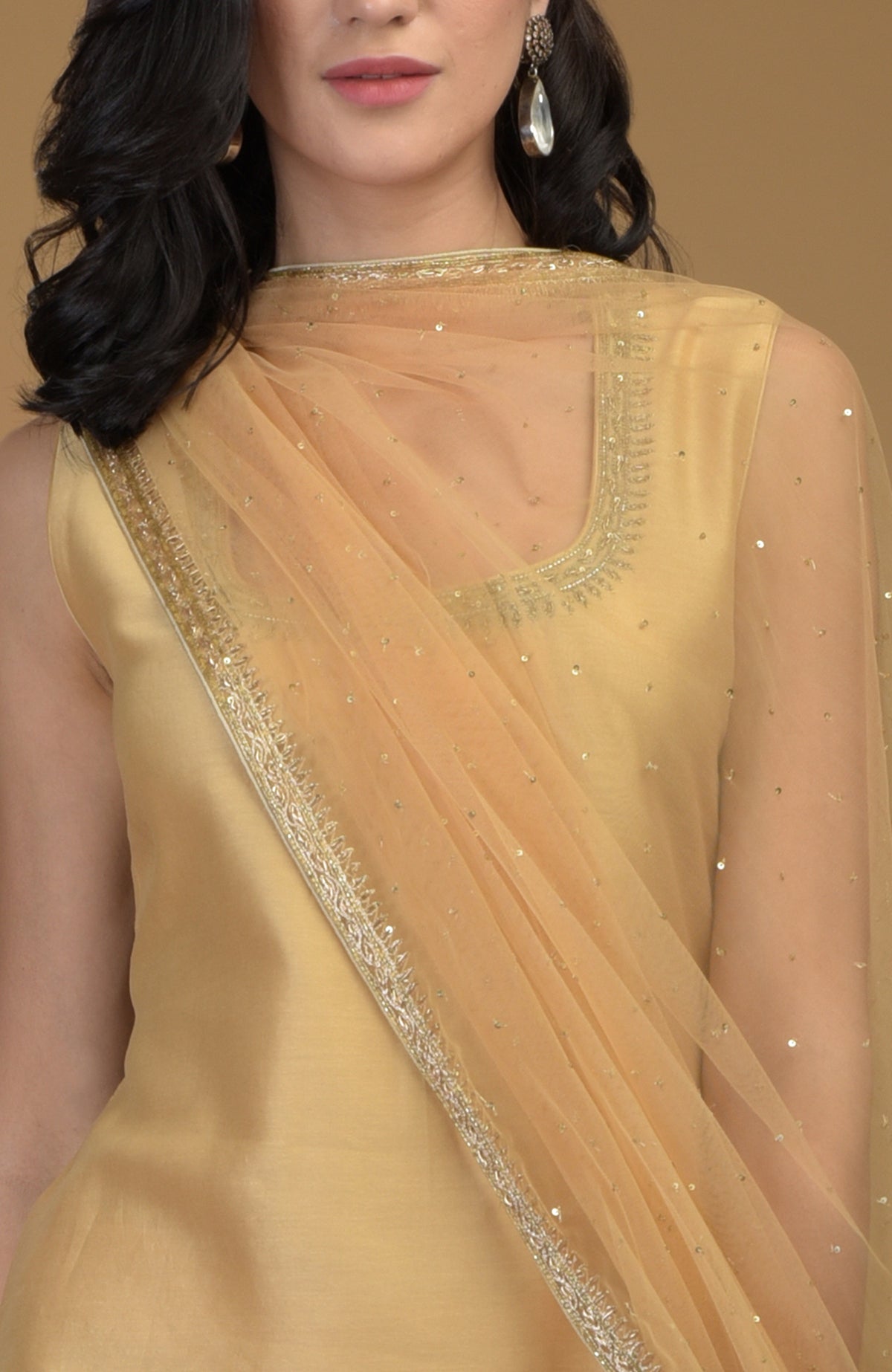 A woman models a nude gold zardozi hand-embroidered suit with a sheer dupatta.