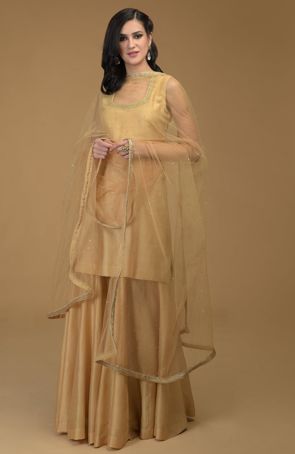 A woman models a nude gold zardozi hand-embroidered gharara suit with a sheer dupatta.