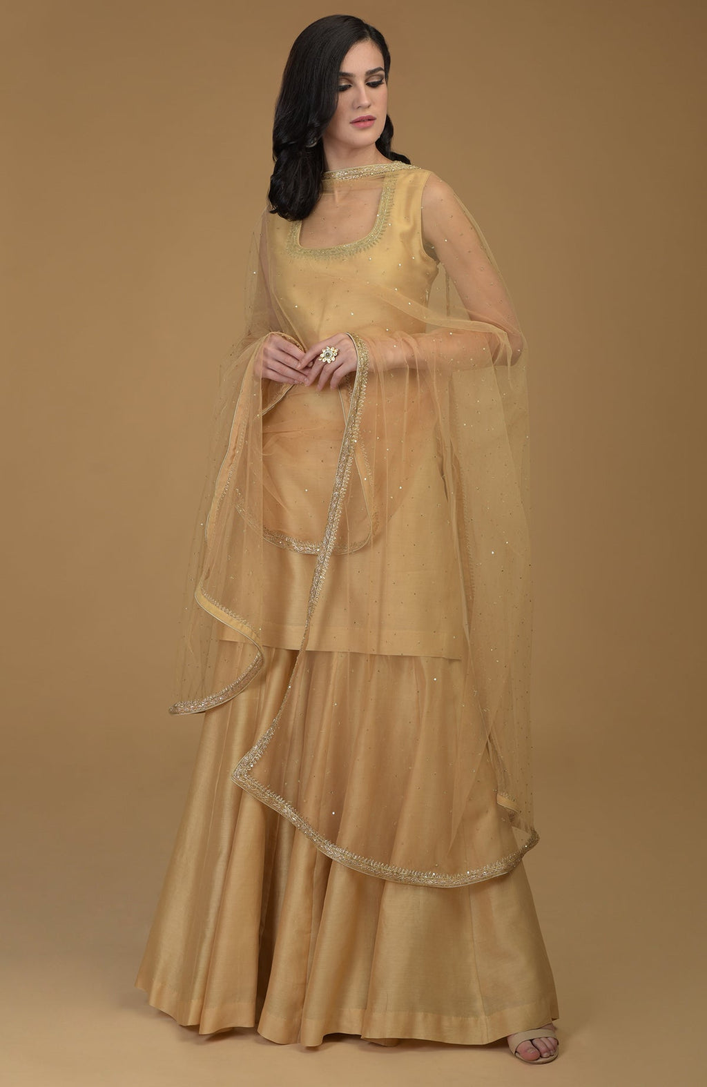 A woman models a nude gold zardozi hand-embroidered gharara suit with a sheer dupatta.