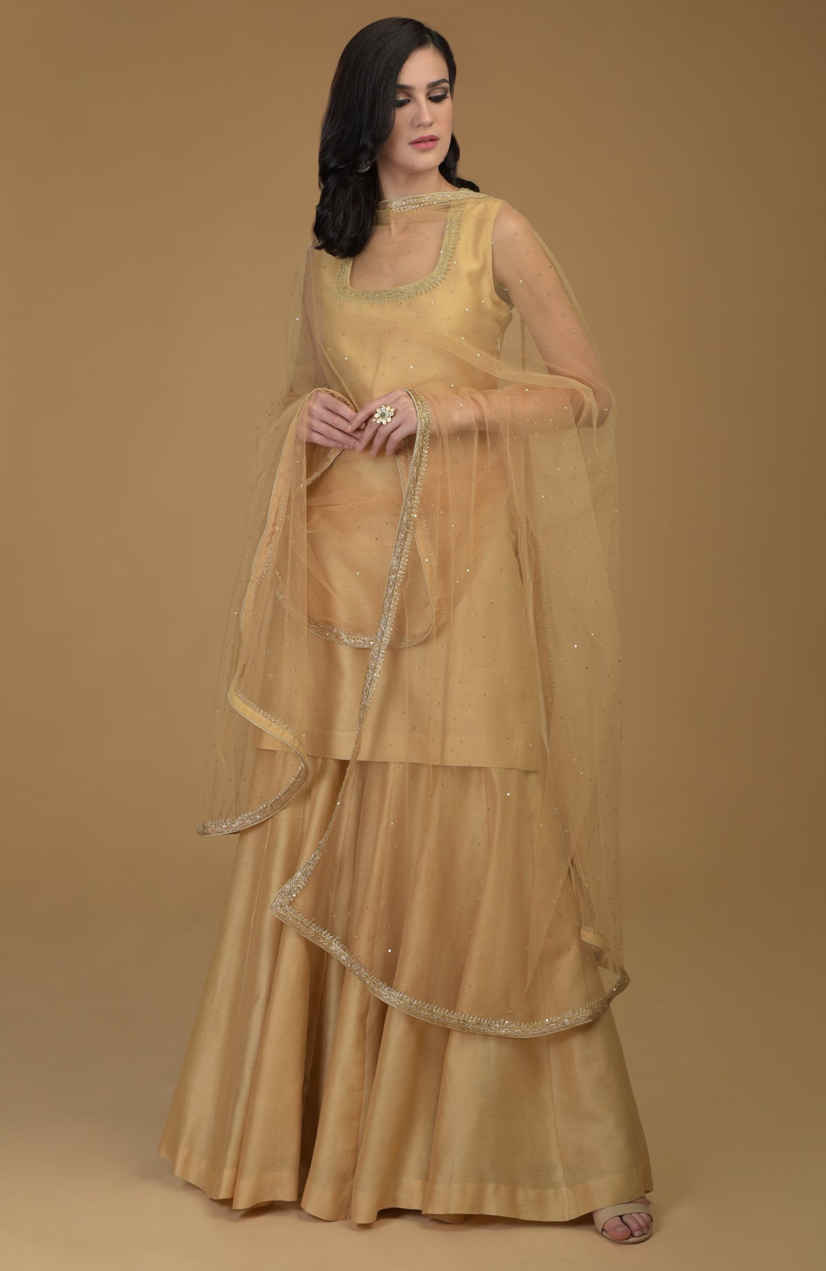 A woman models a nude gold zardozi hand-embroidered gharara suit with a sheer dupatta.