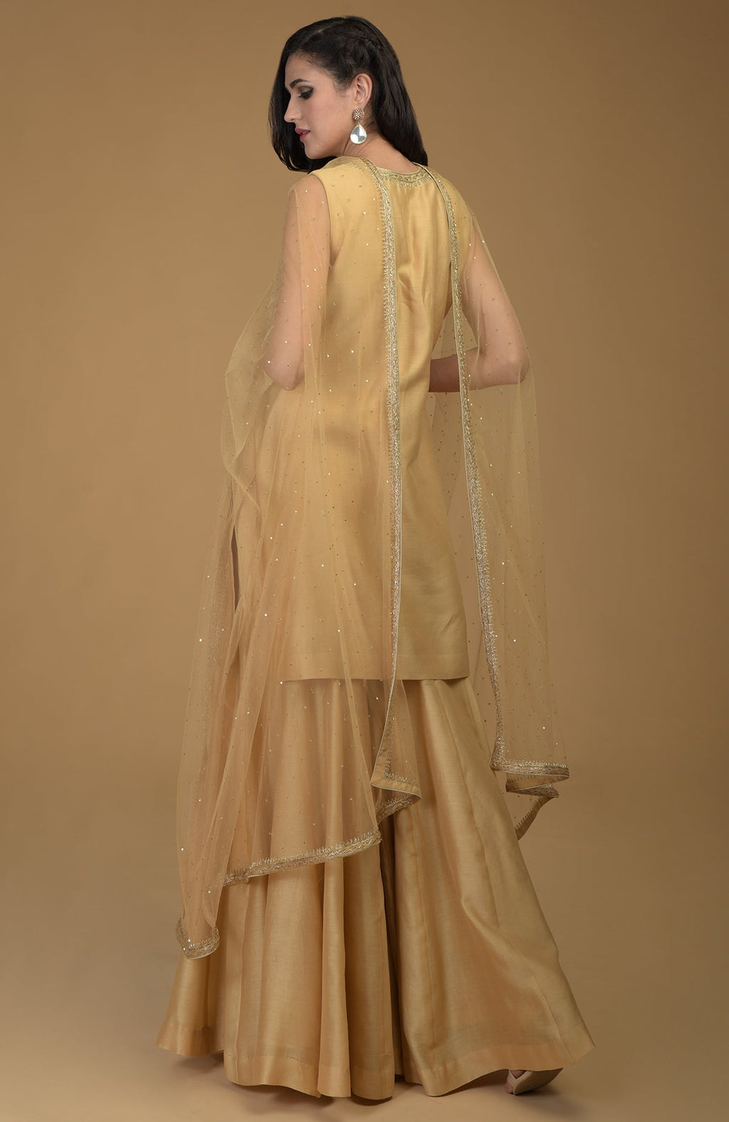 A woman models a nude gold zardozi hand embroidered gharara suit with a sheer dupatta.