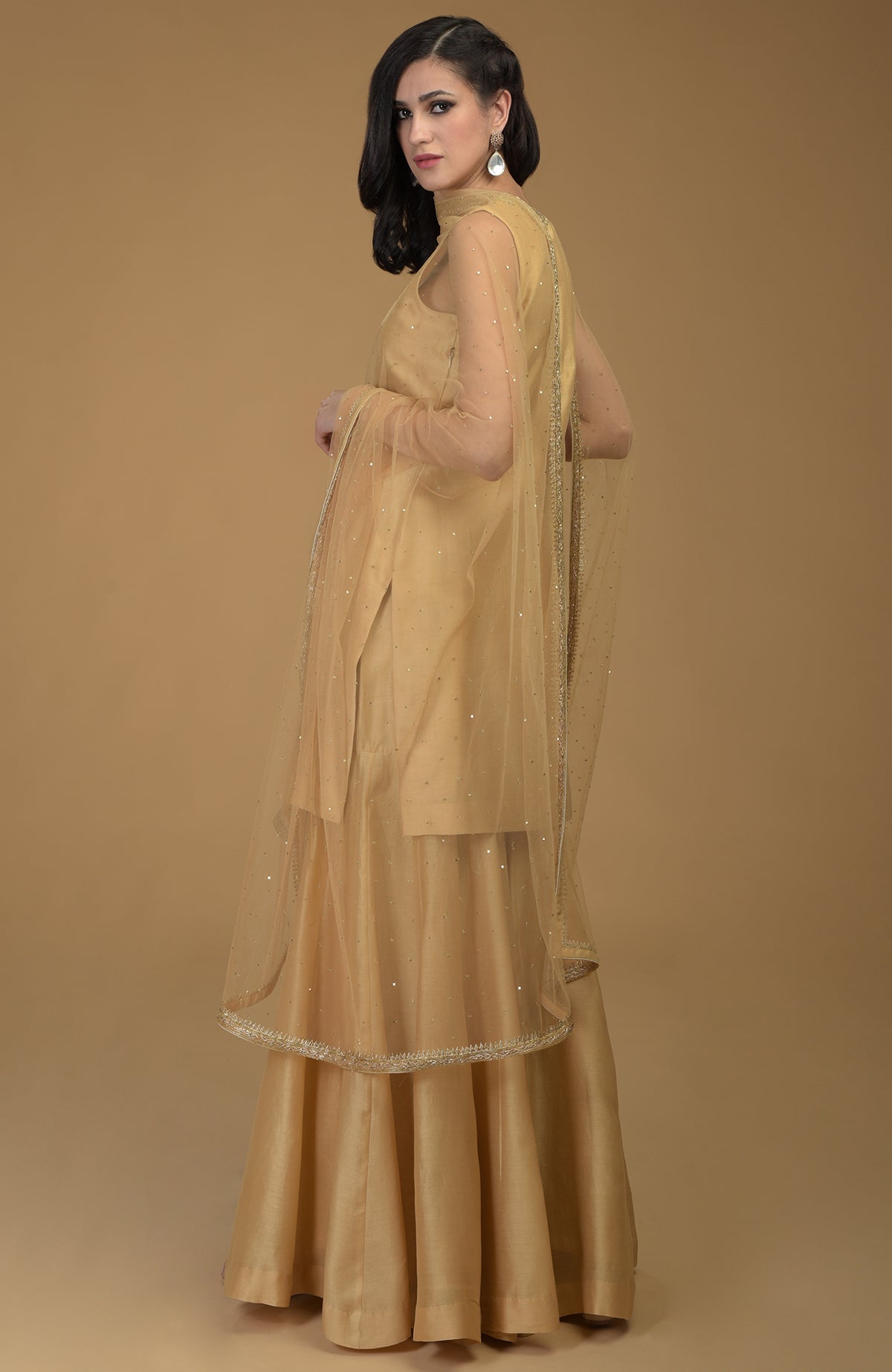 A woman models a nude gold zardozi hand-embroidered gharara suit with a sheer dupatta.