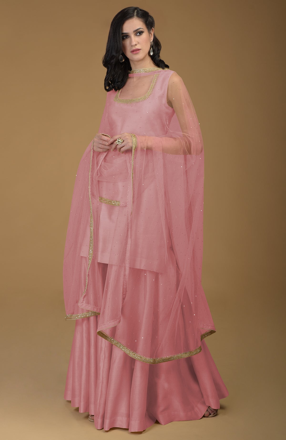 A woman models a ruby red gharara suit with gold zardozi embroidery.