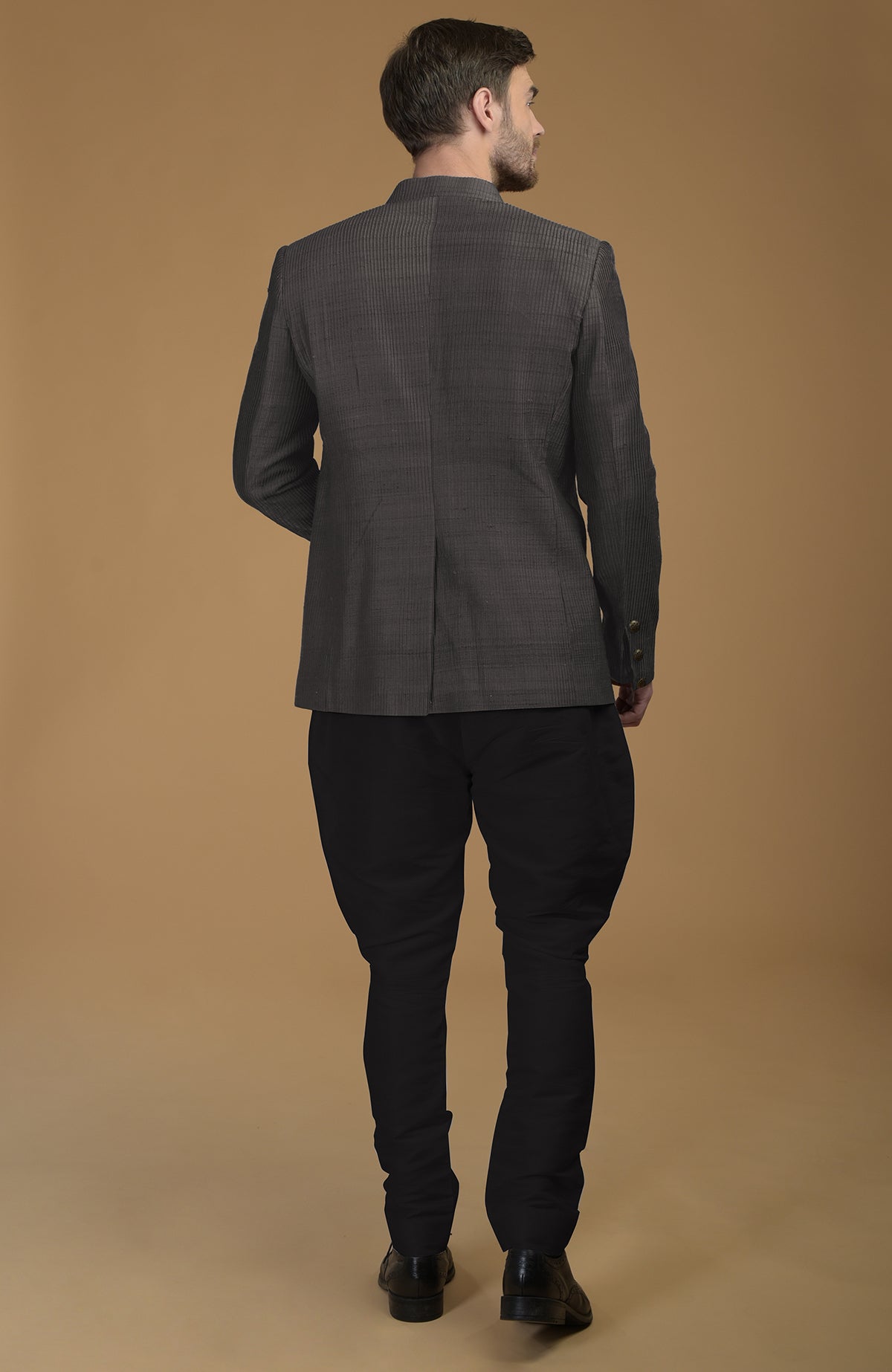Charcoal grey pintuck raw silk bandhgala jacket with black pants, viewed from the back.