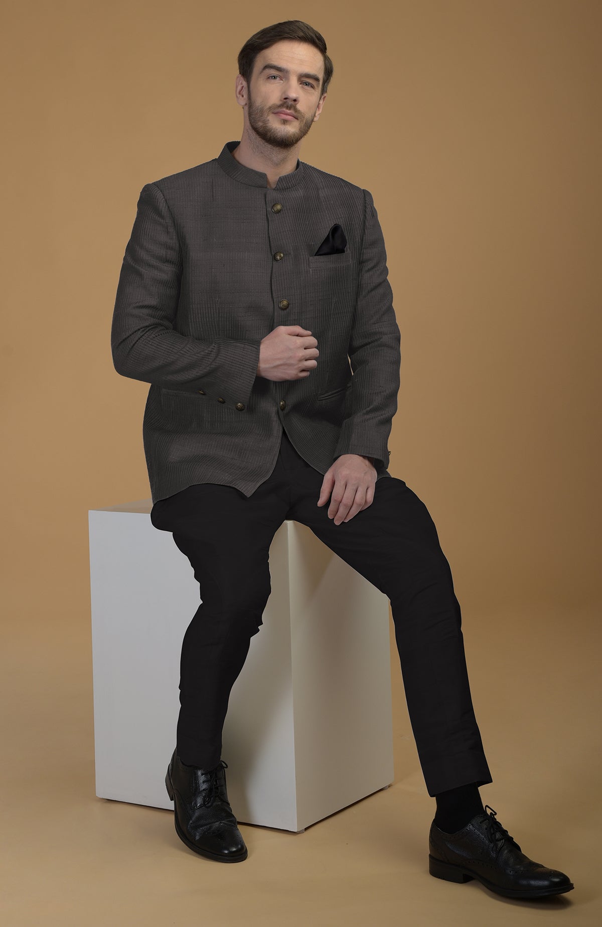 A man models a charcoal grey pintuck pure raw silk bandhgala jacket set.