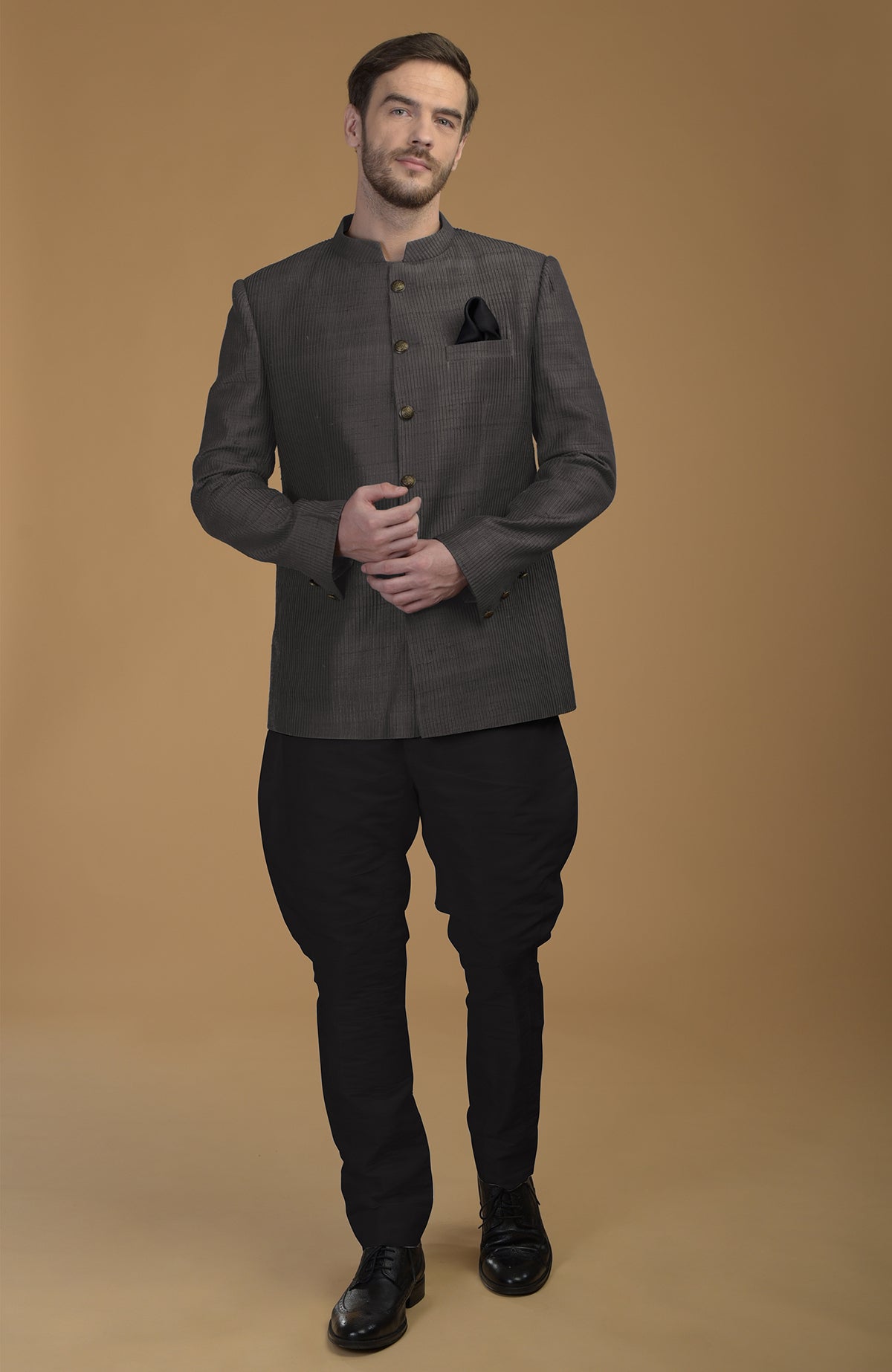 A man models a charcoal grey pintuck raw silk Bandhgala jacket and black Jodhpuri pants.