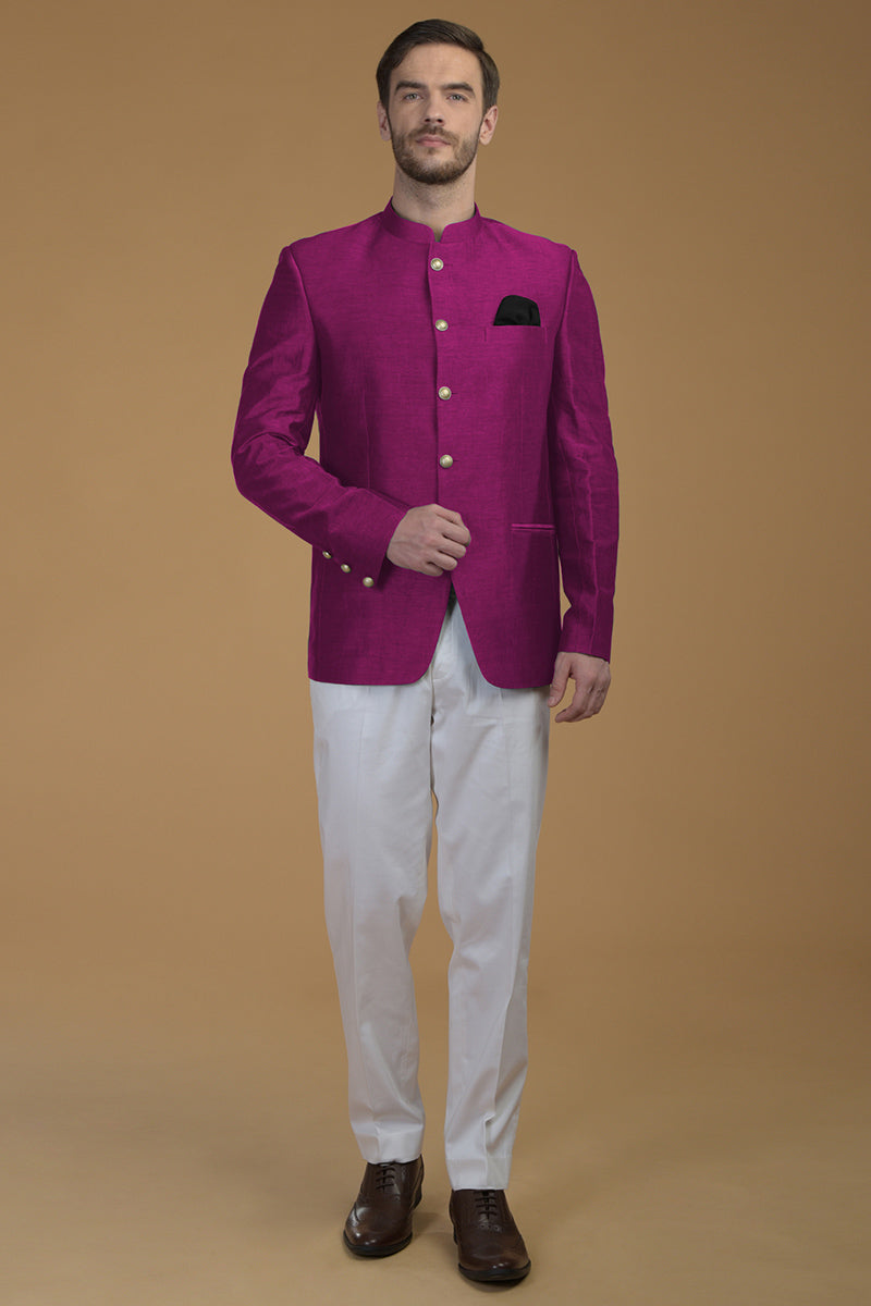 A man models a peacock pink linen silk bandhgala jacket with white pants and brown shoes.