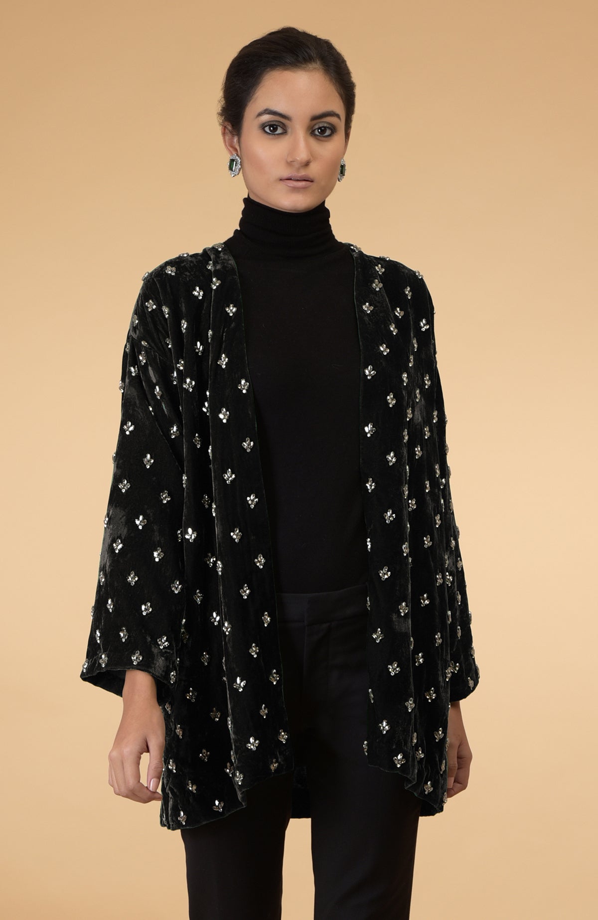 A woman models a dark olive crystal hand-embroidered silk velvet jacket over a black turtleneck.
