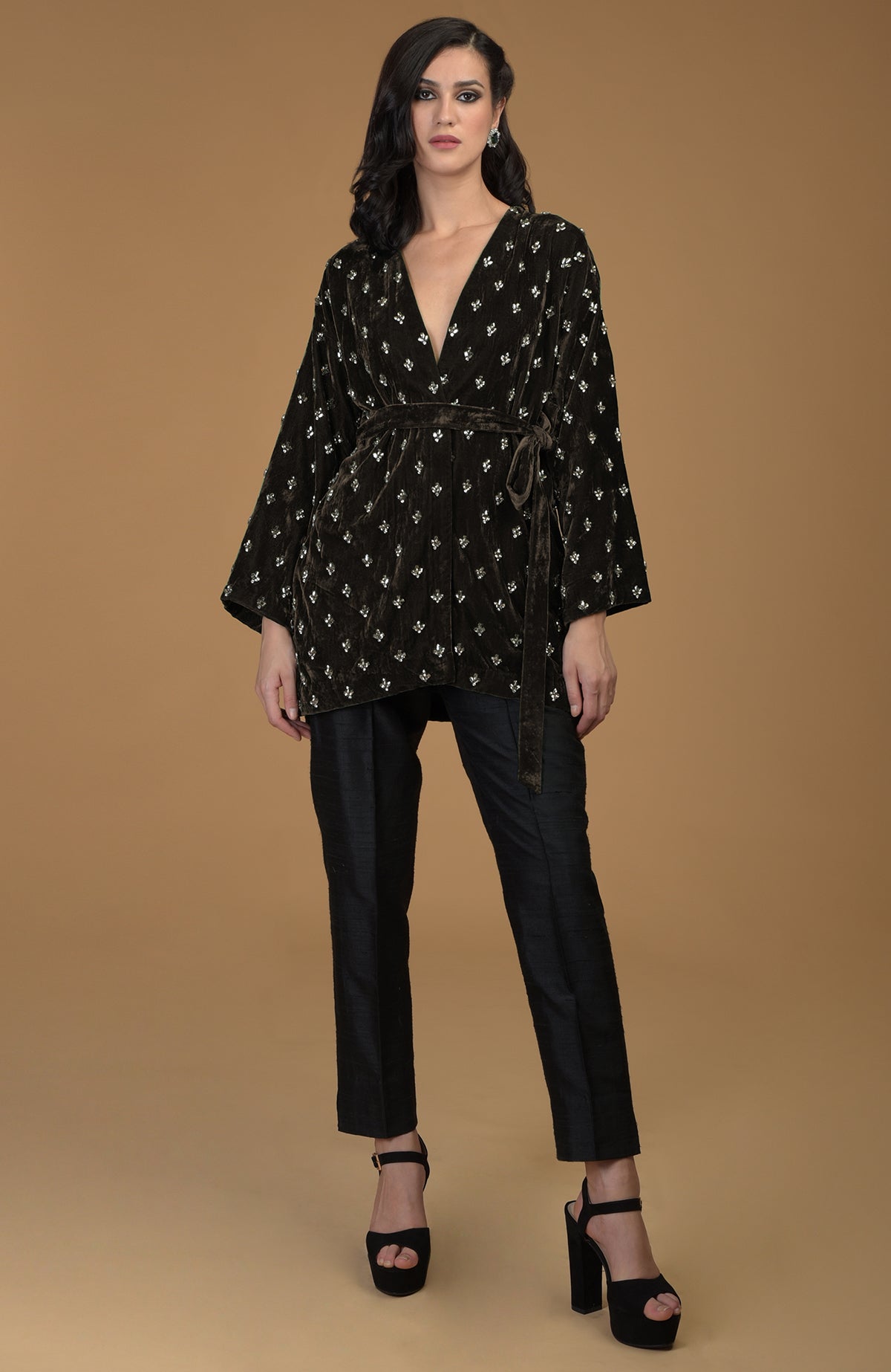 A woman models a dark olive silk velvet jacket with crystal embroidery and black pants.