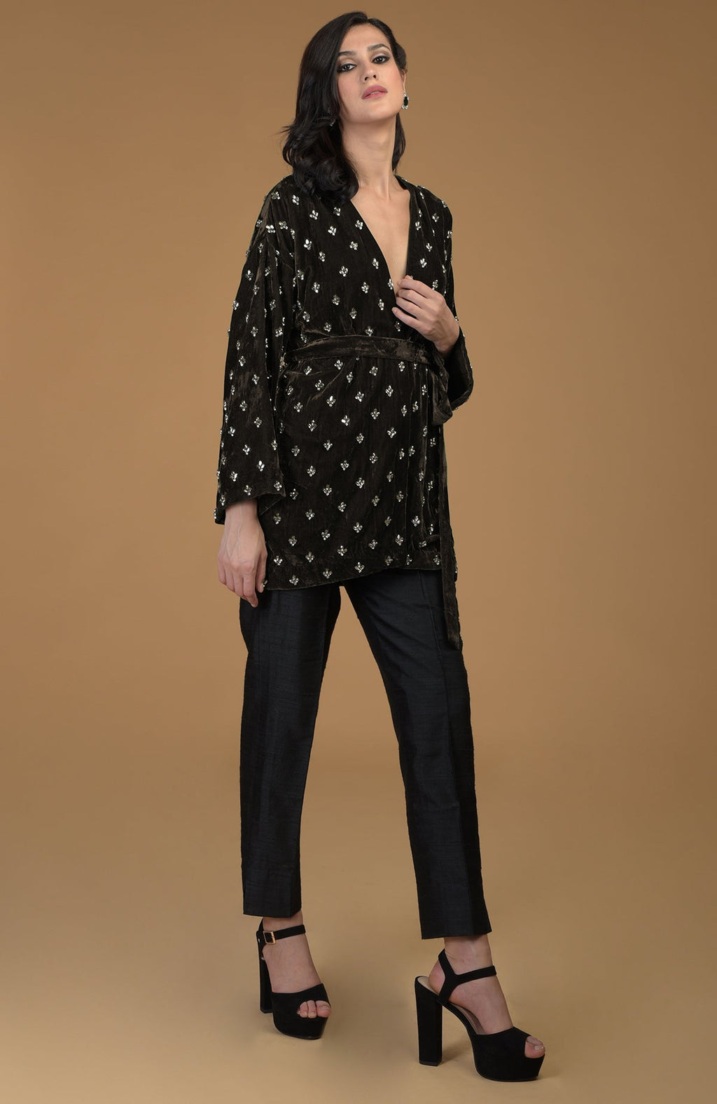 A woman models a dark olive crystal hand-embroidered silk velvet jacket and black pants.