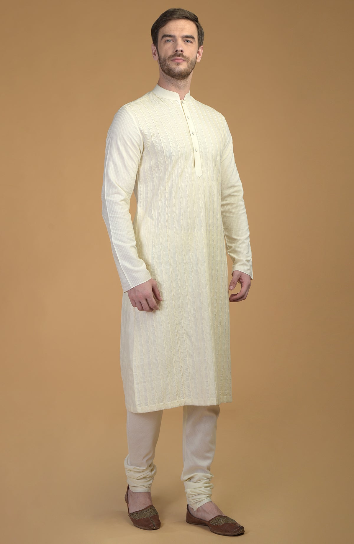 Cream kurta with pintuck and Kantha detail, paired with matching churidar and brown juttis.