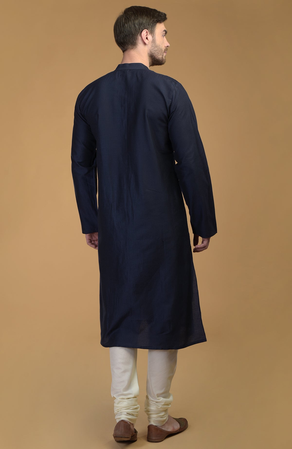 A man from behind wears a dark navy kurta with pintuck and kantha detail and ivory churidars.