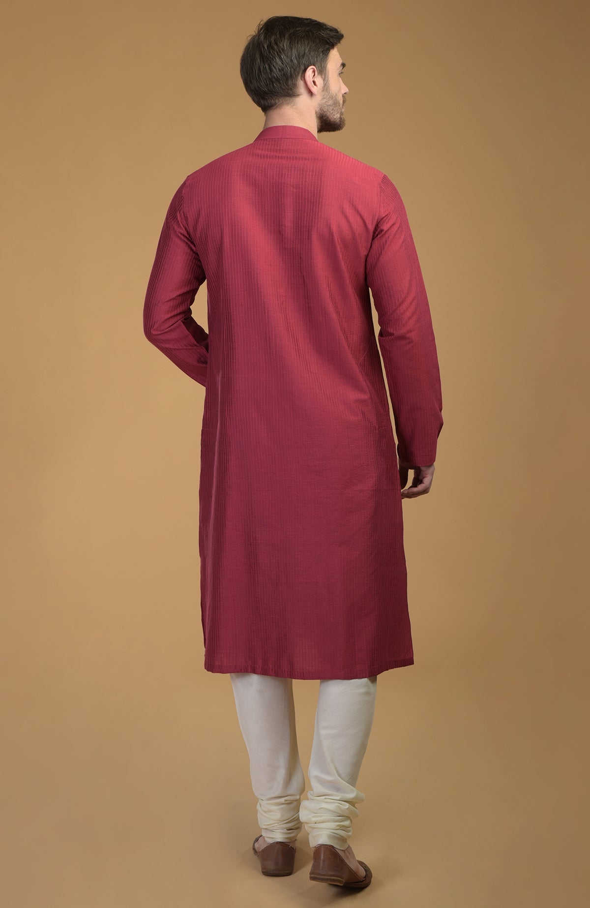 A man from behind wears a wine kurta with pintuck and kantha detail and ivory churidars.