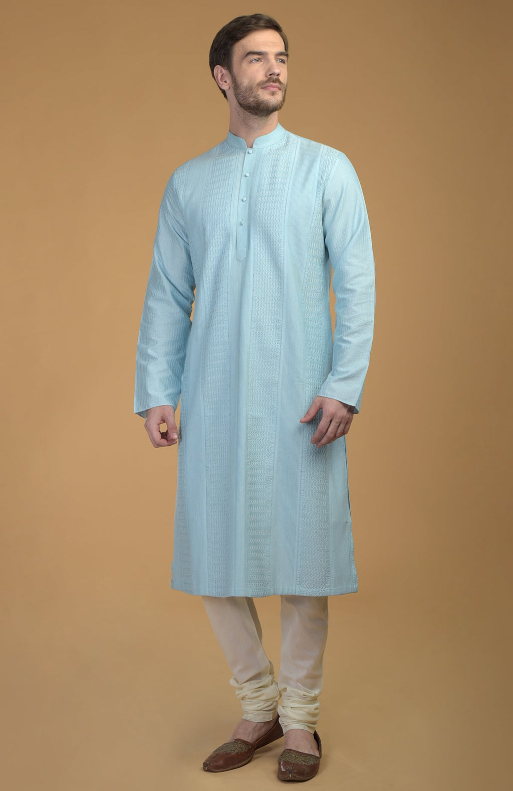 A man stands wearing an ice blue kurta with pintuck and kantha details and ivory churidars.