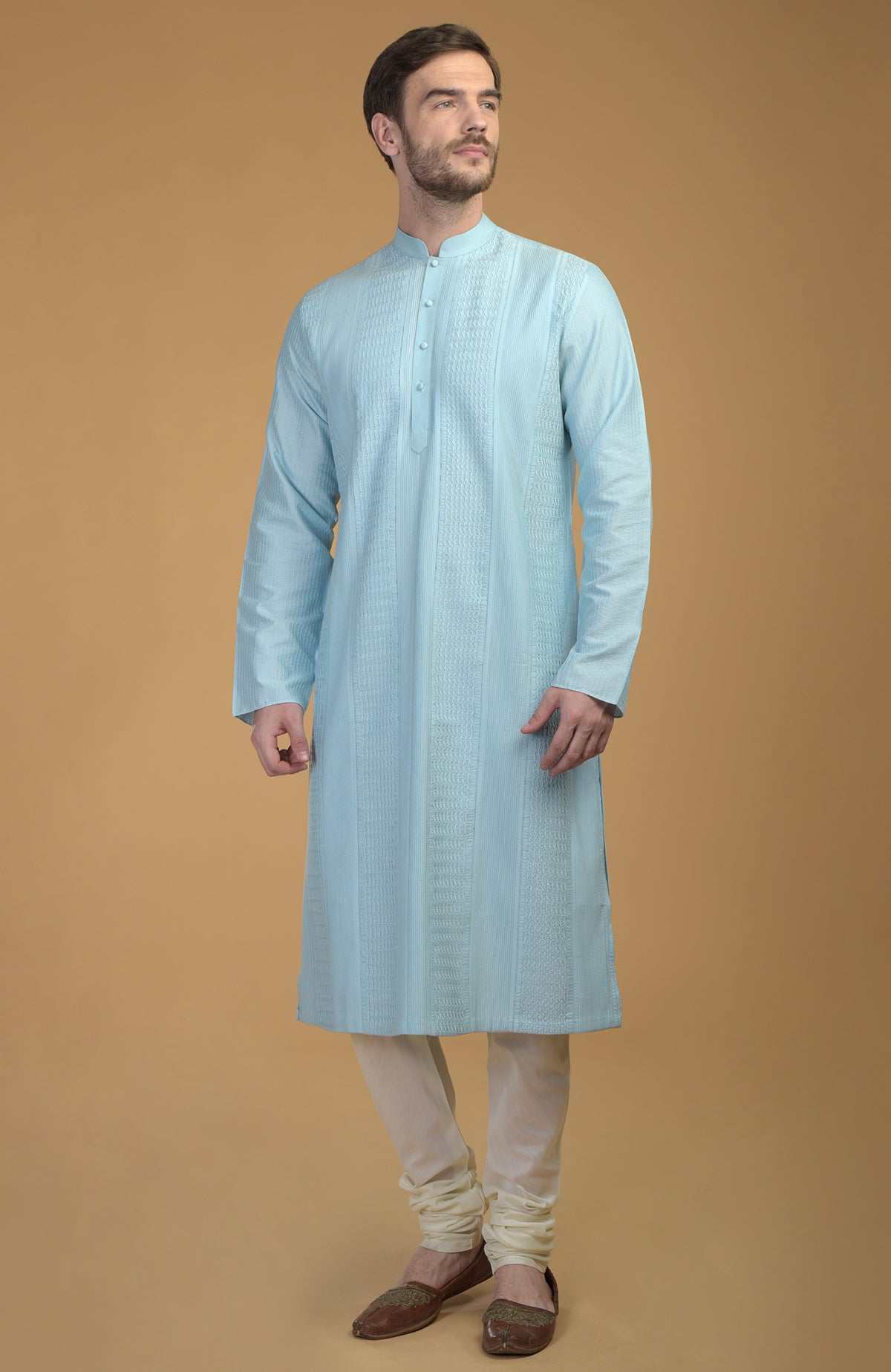 A man stands wearing an ice blue kurta with pintuck and kantha details and ivory churidars.