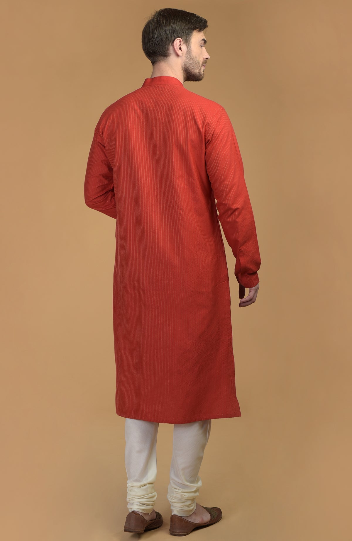 A man from behind wearing a red kurta with pintuck and kantha details, and ivory churidars.