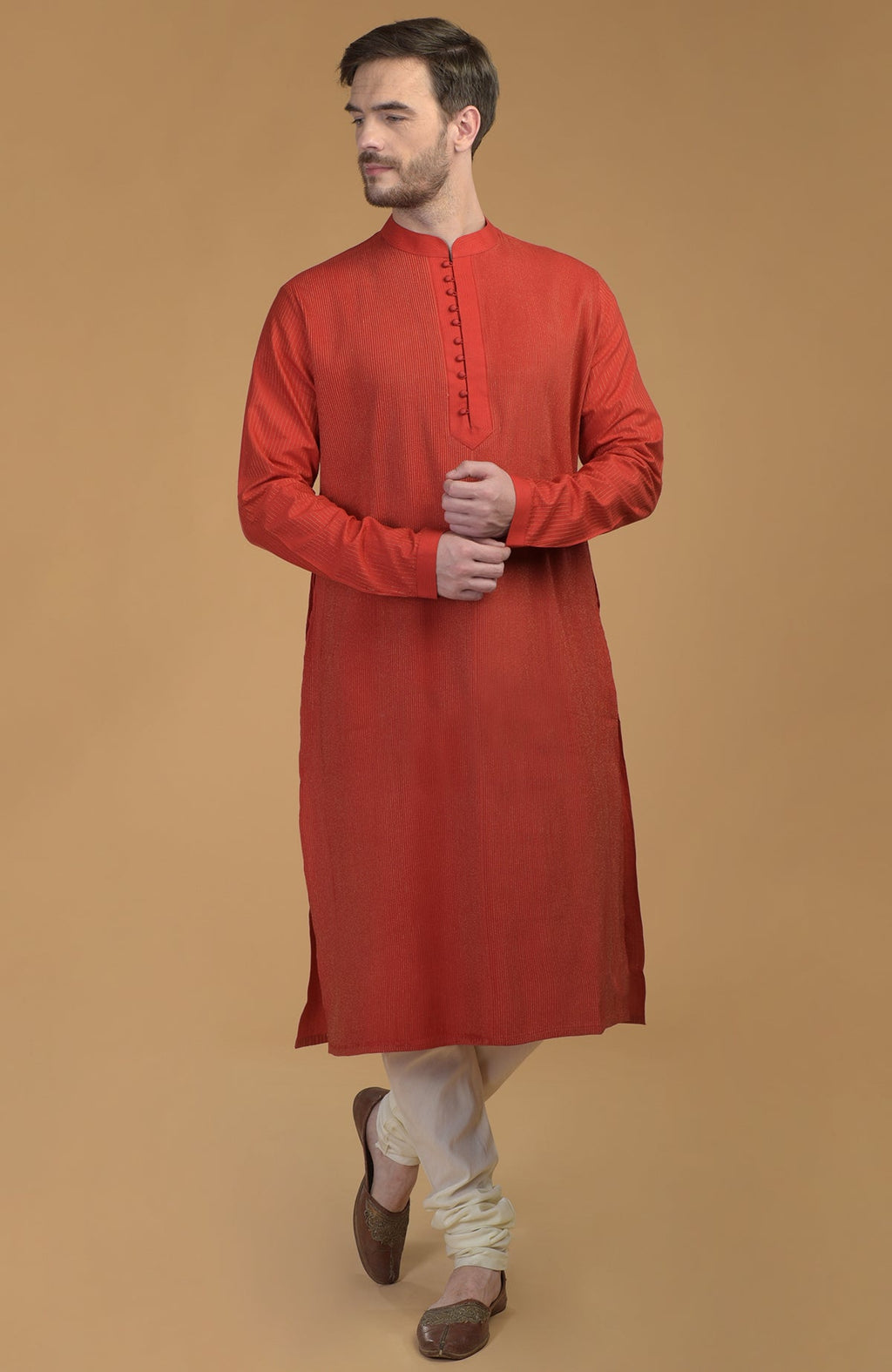 A man models a red kurta with pintuck and kantha details and ivory churidars.