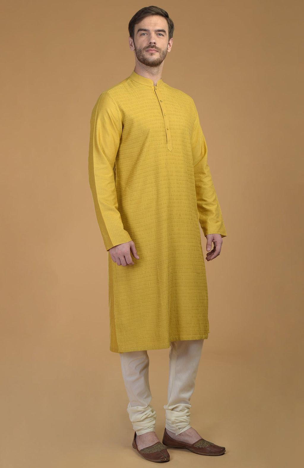 A man models a sunglow yellow kurta with pintuck and kantha details and ivory churidars.