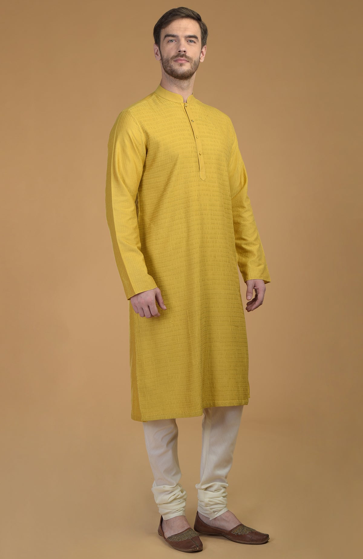 A man models a sunglow yellow kurta with pintuck and kantha details and ivory churidars.