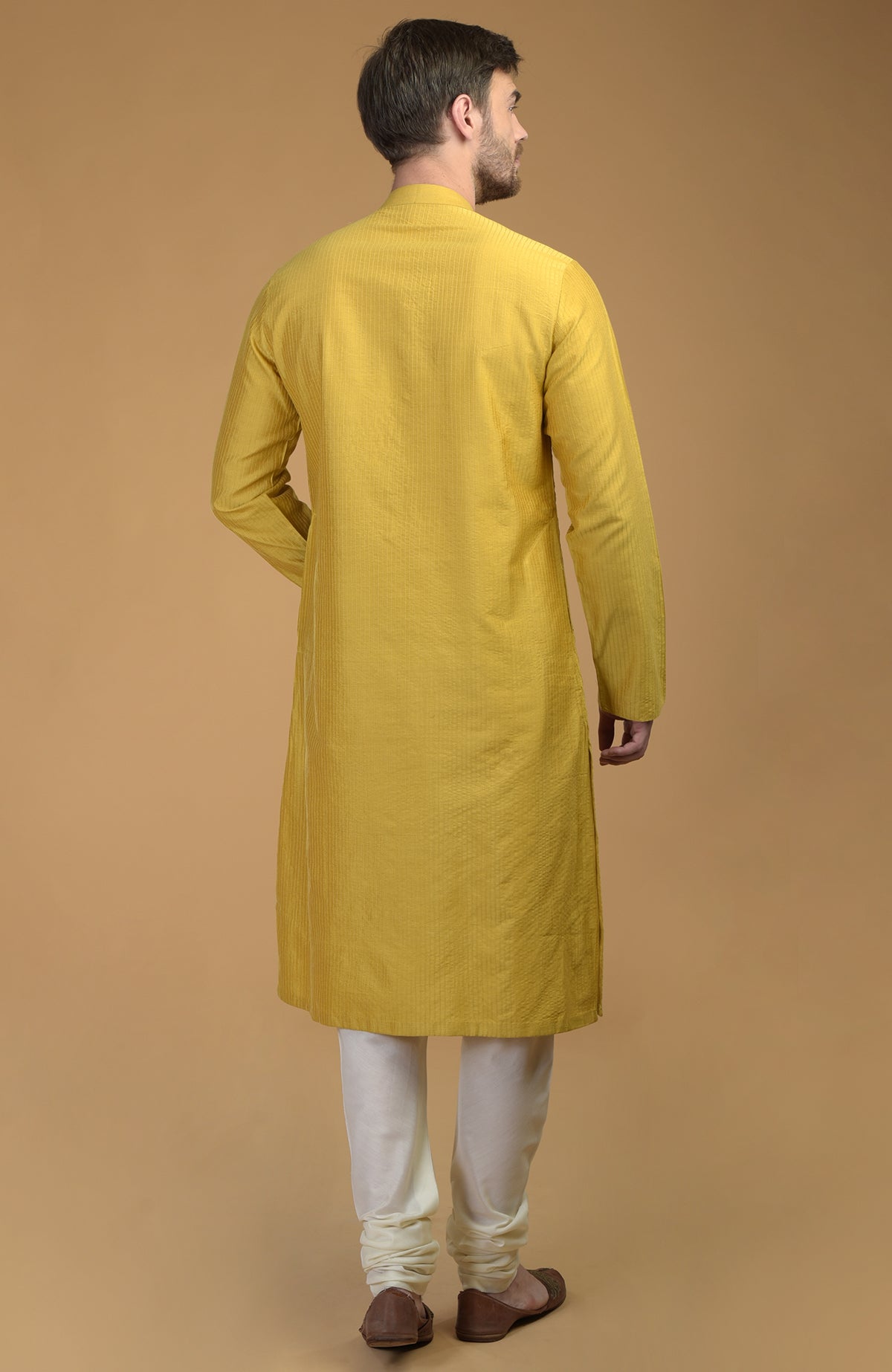 A man from behind wears a yellow kurta with pintuck and kantha details and white churidar.