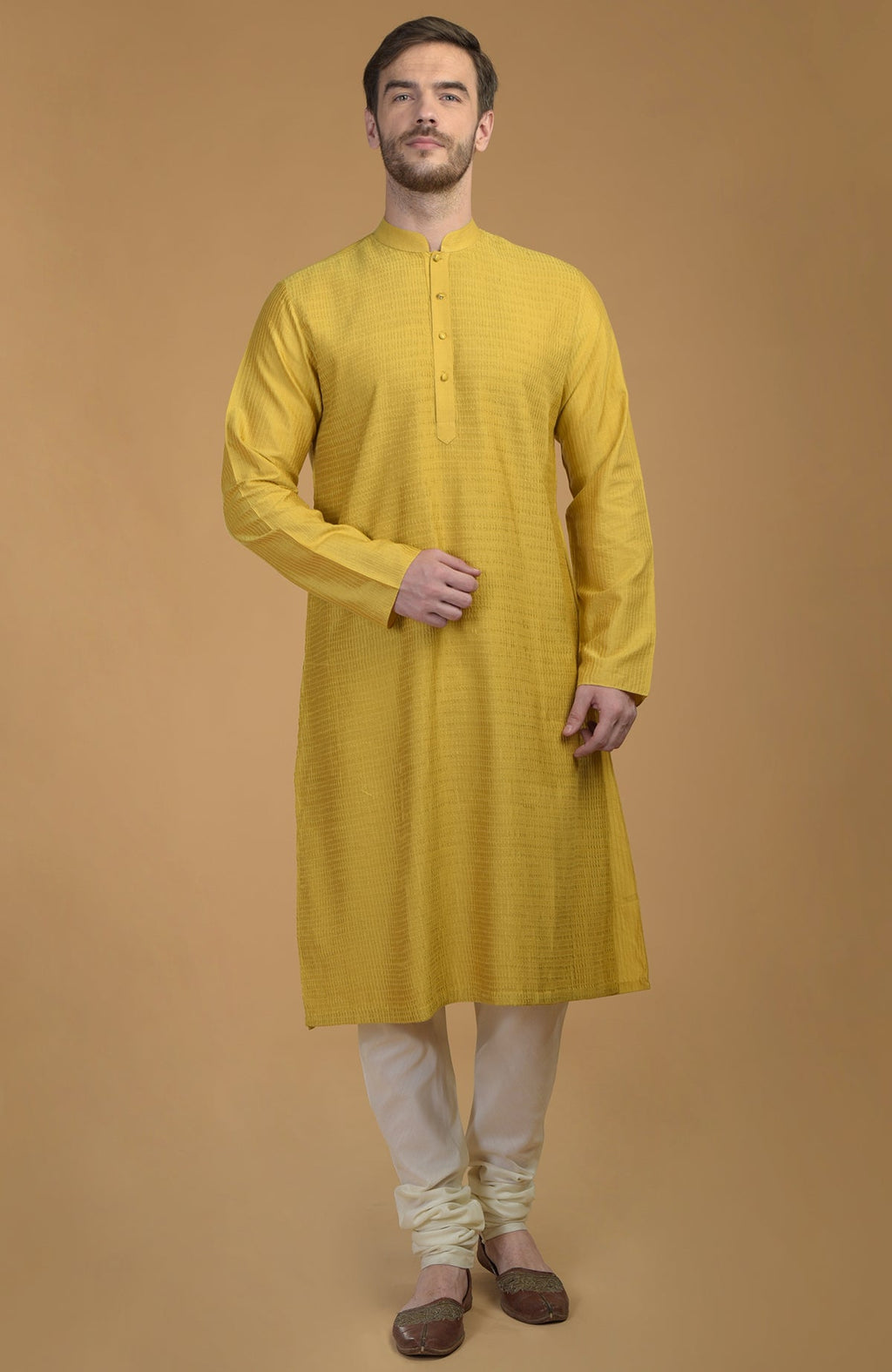 A man models a sunglow yellow kurta with pintuck and kantha detail, and ivory churidar pants.