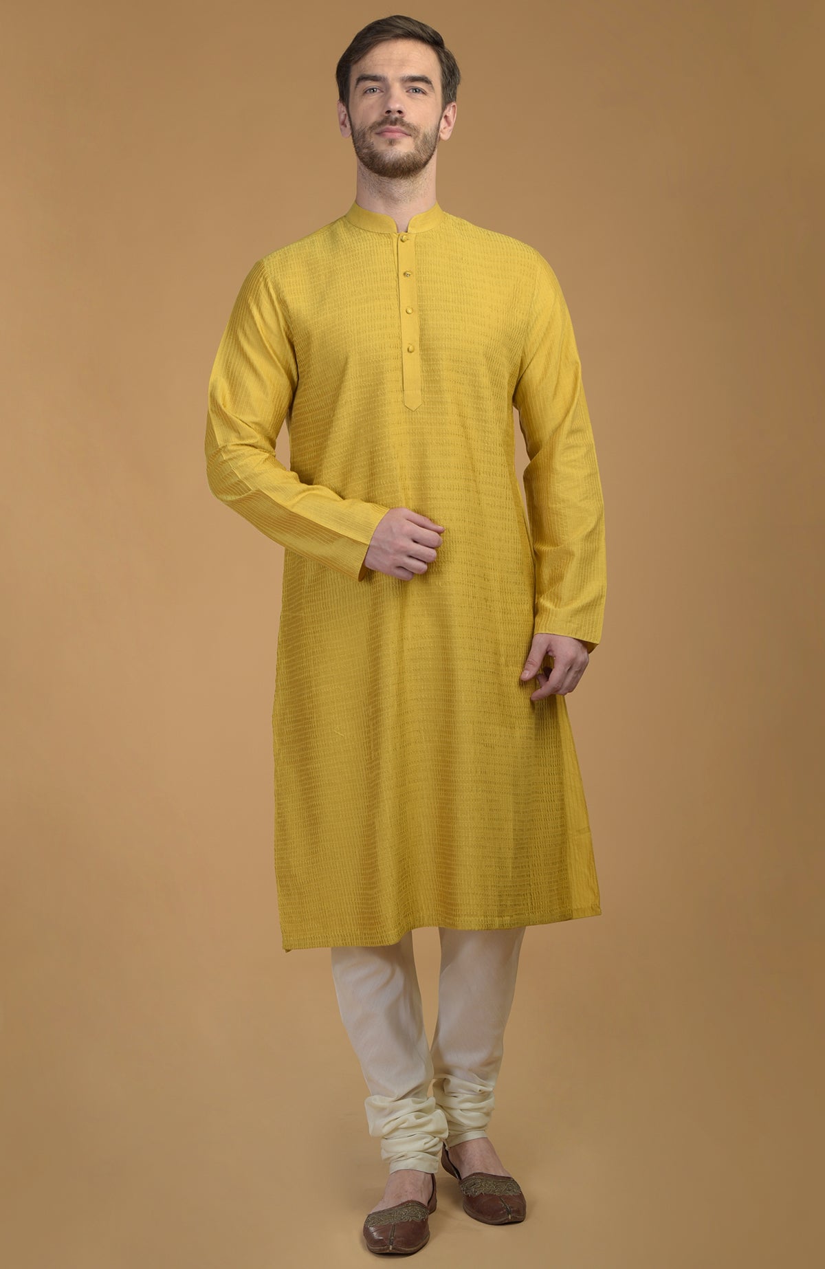 A man models a sunglow yellow kurta with pintuck and kantha detail, and ivory churidar pants.