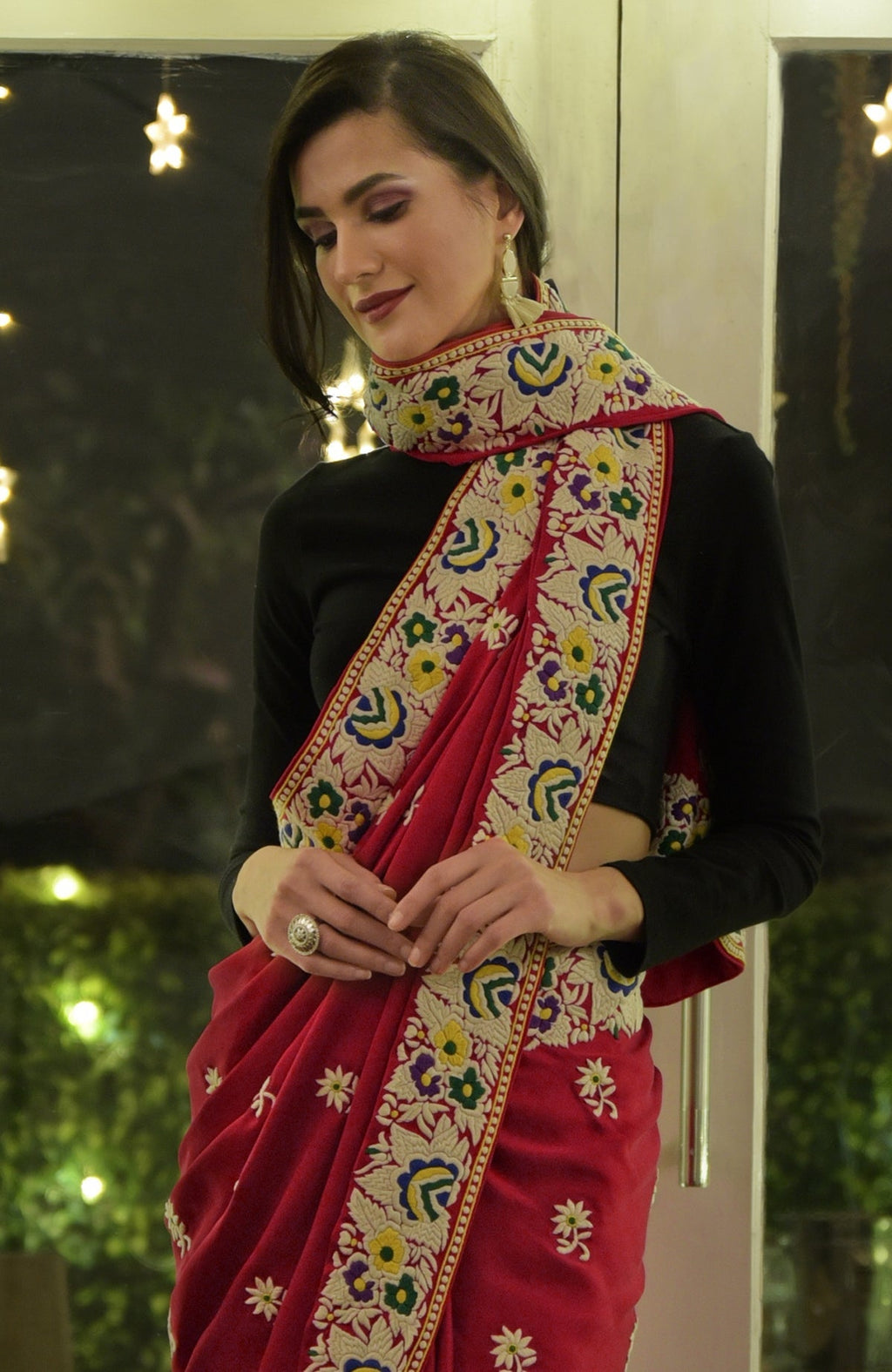 A woman models a red Parsi Gara hand-embroidered saree with a black blouse.