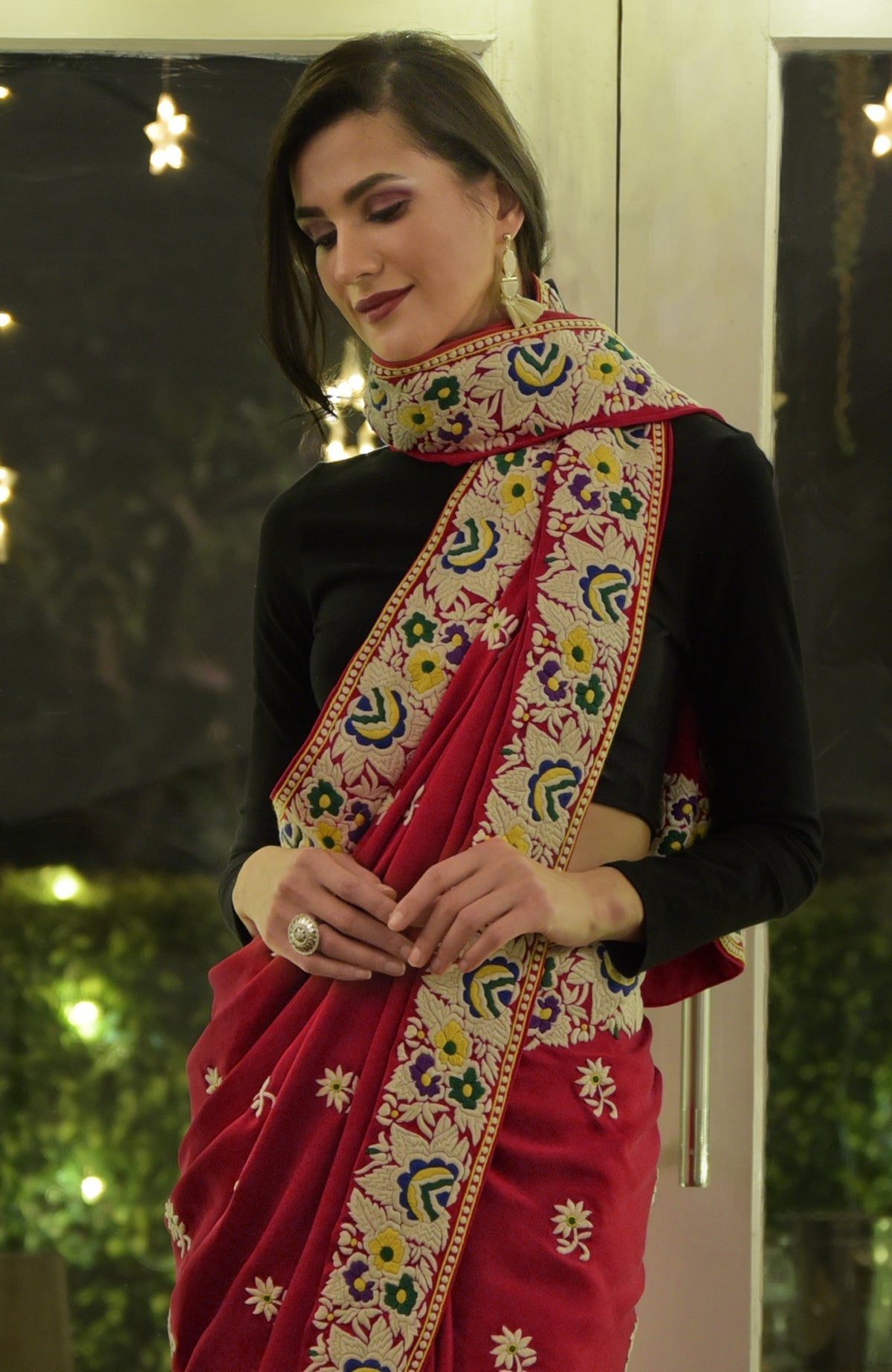 A woman models a red Parsi Gara hand-embroidered saree with a black blouse.
